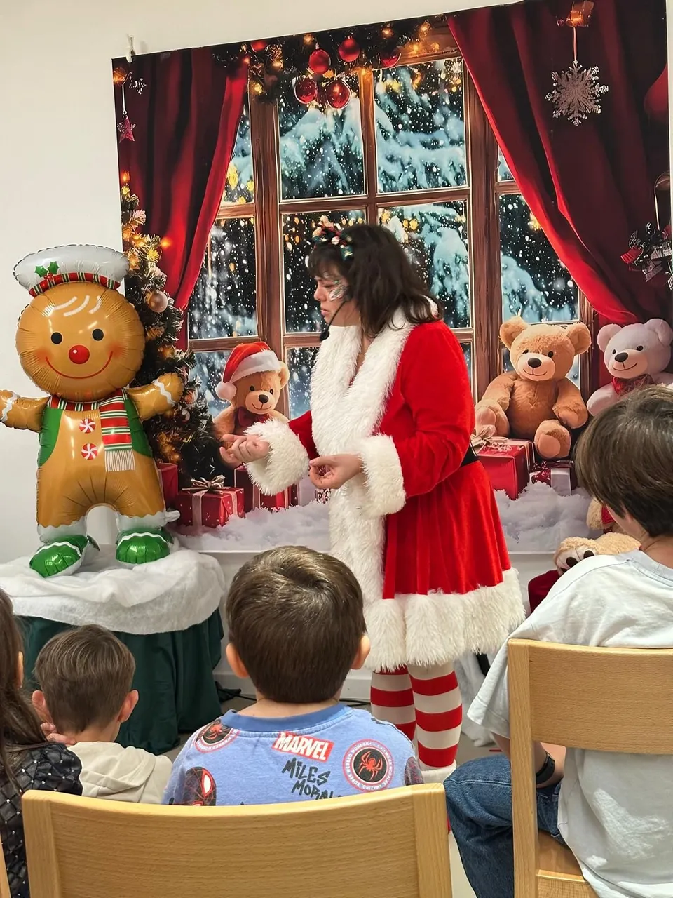 Berce en Mère Noël devant des enfants, dans un décor de Noël
